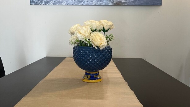 Ett matbord med en vas med vita blommor och en målning som föreställer ett kustlandskap, placerad ovanför bordet.