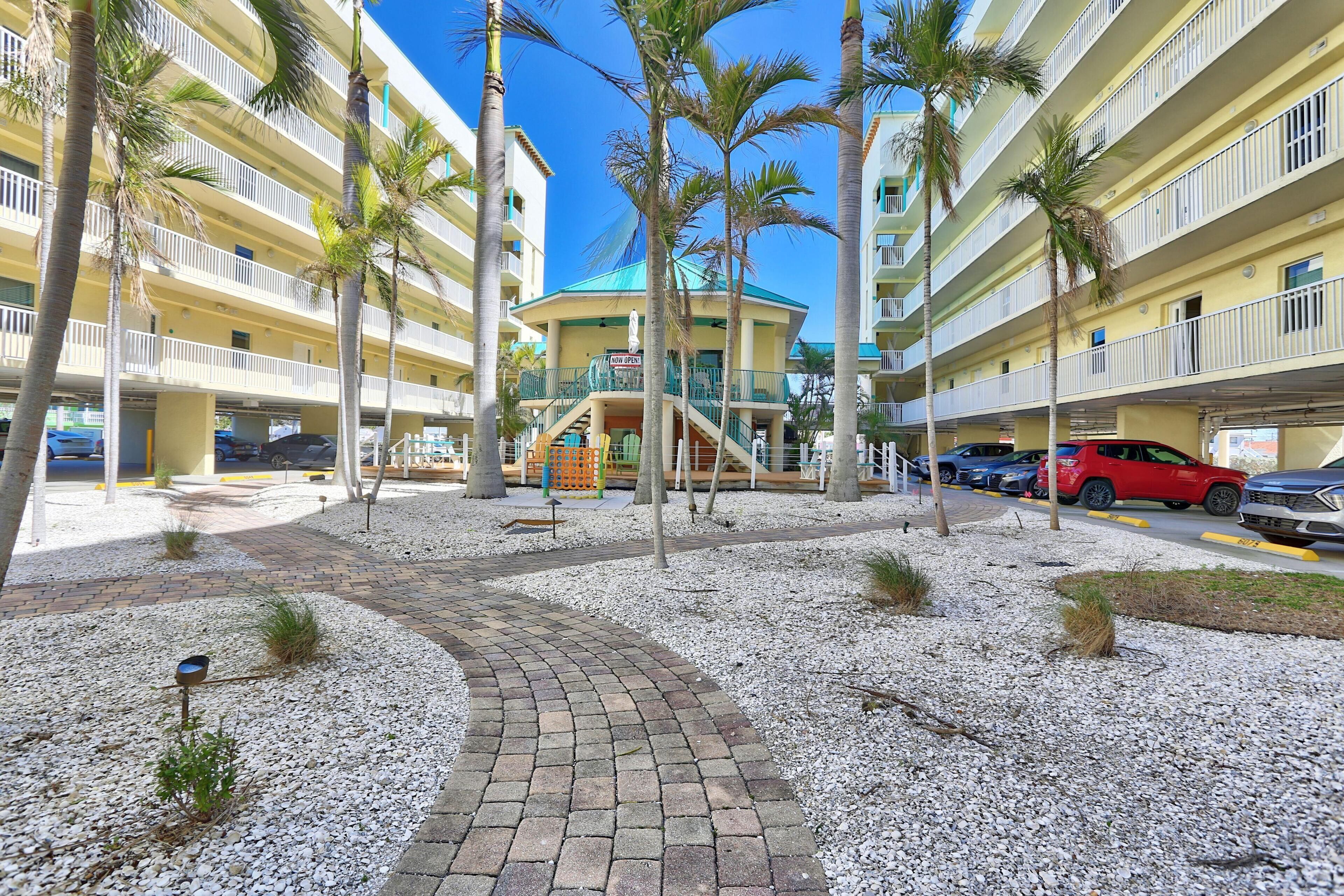 A multi-story hotel with a central atrium, palm trees, and a parking area with several cars.