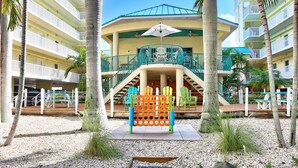 A multi-story hotel with balconies, a central courtyard with a play structure, and palm trees. - Sunset Vistas 211n (Treasure Island)