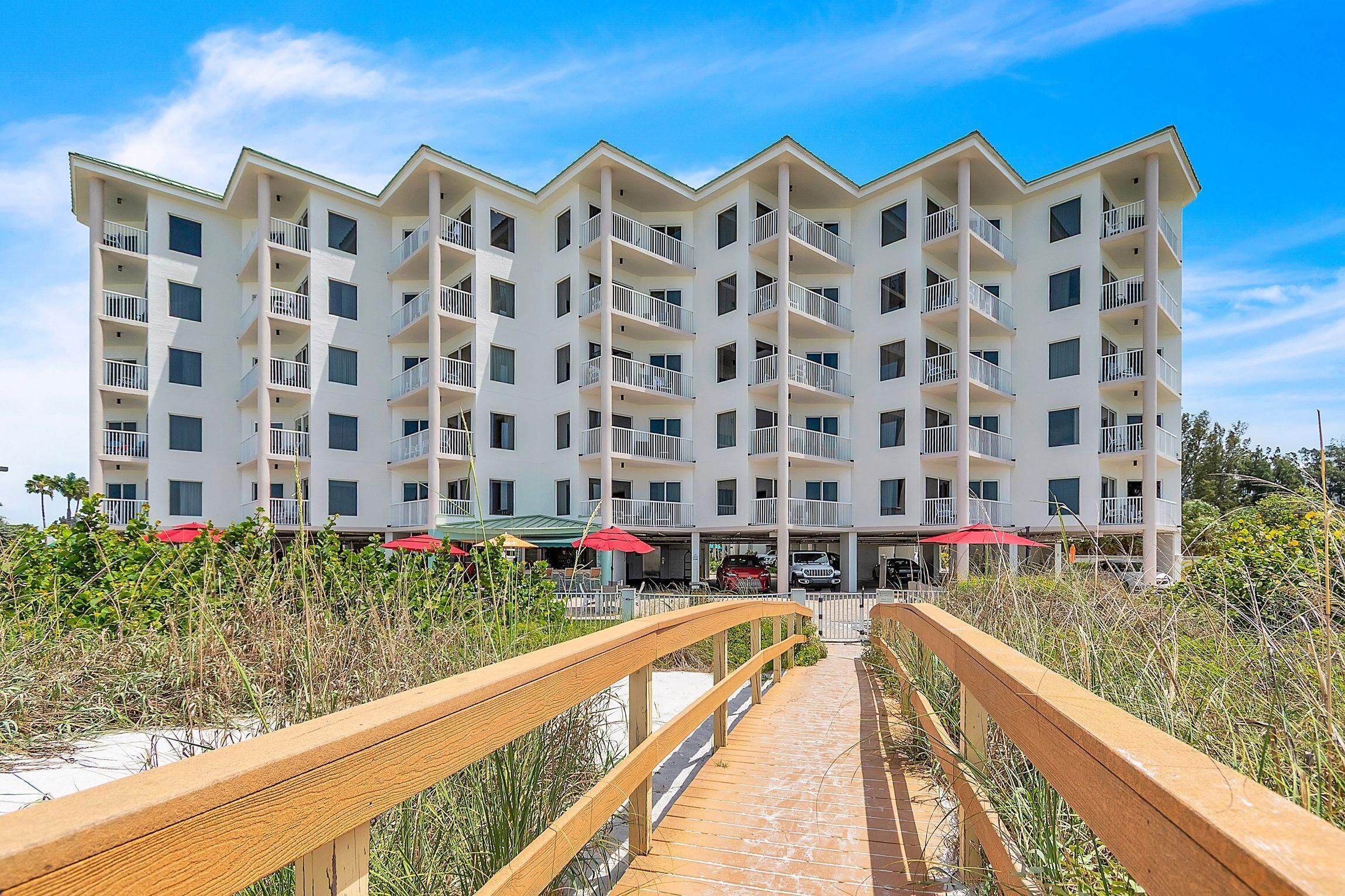A multi-story hotel with balconies, a wooden walkway, and outdoor umbrellas.