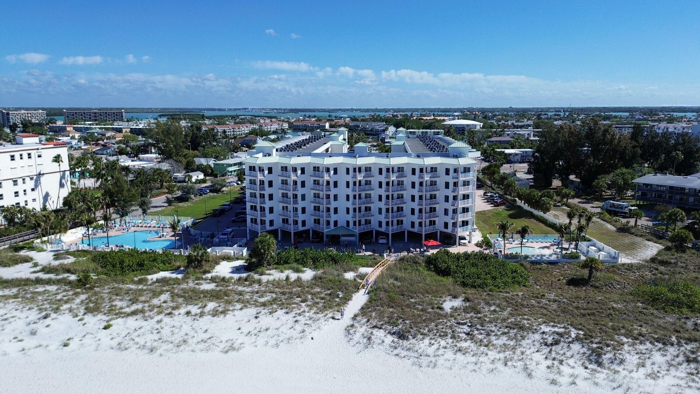 A multi-story hotel with a pool, surrounded by greenery and a beach.