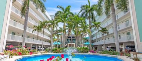 Ett hotell med en pool i mitten, omgivet av palmer och balkonger.