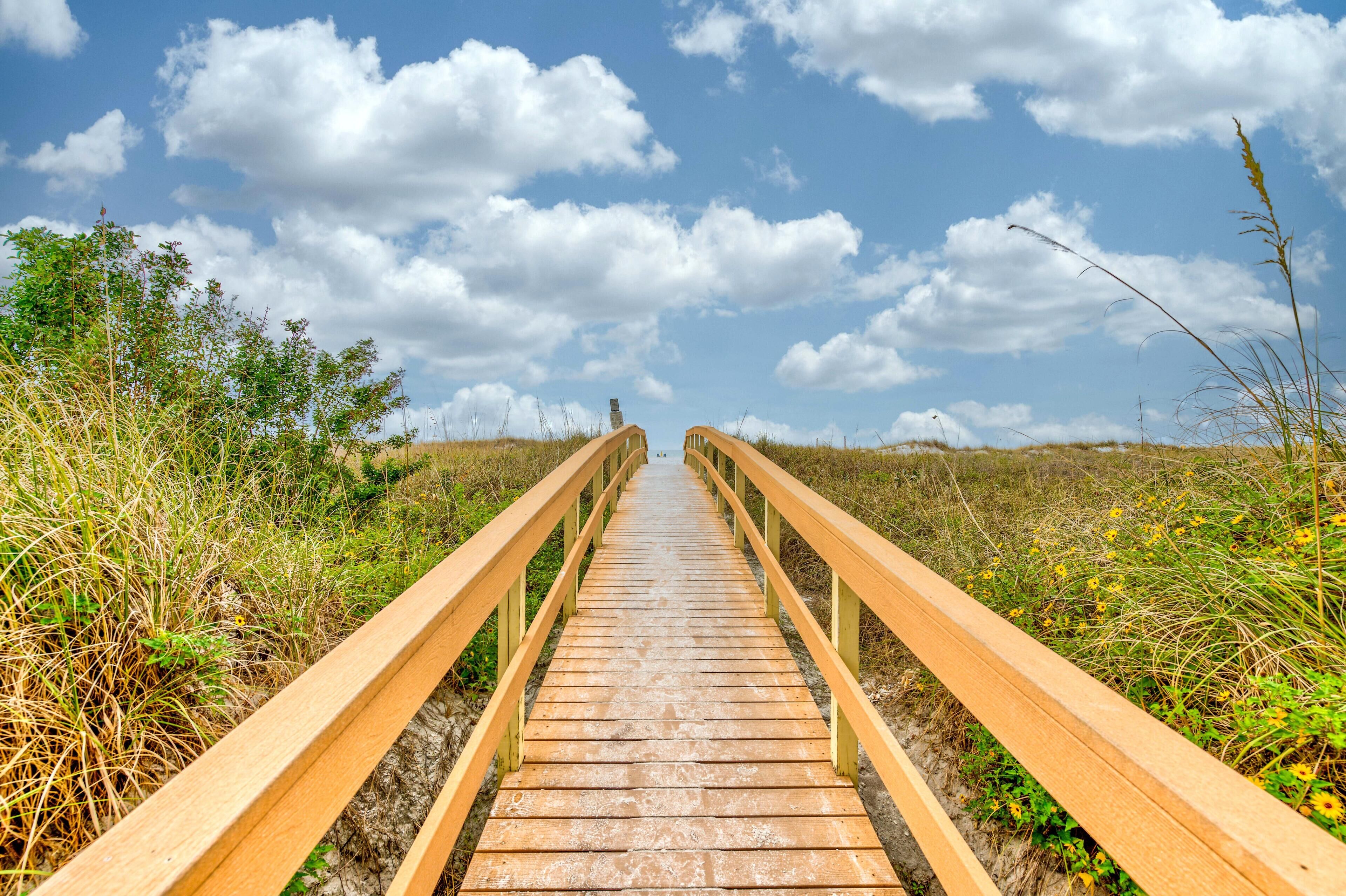 A wooden boardwalk leading to a building with a chimney, surrounded by vegetation.
