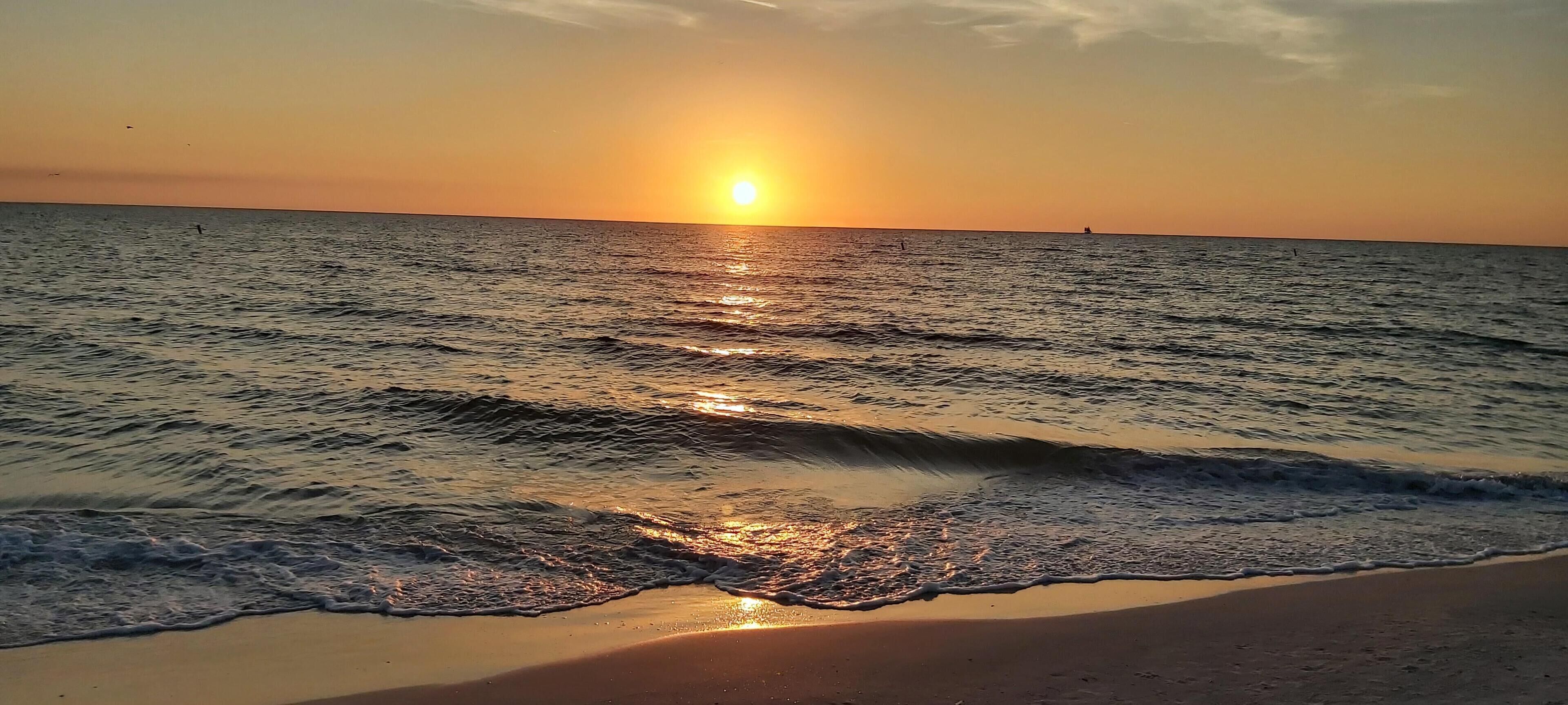 Escena de playa con olas y un atardecer.