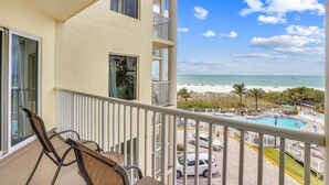 Un balcon donnant sur une plage, une piscine et des voitures garées.