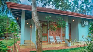 A two-story building with a covered porch, two lounge chairs, and a brick wall. - Villa Mandari (Dharga Town)