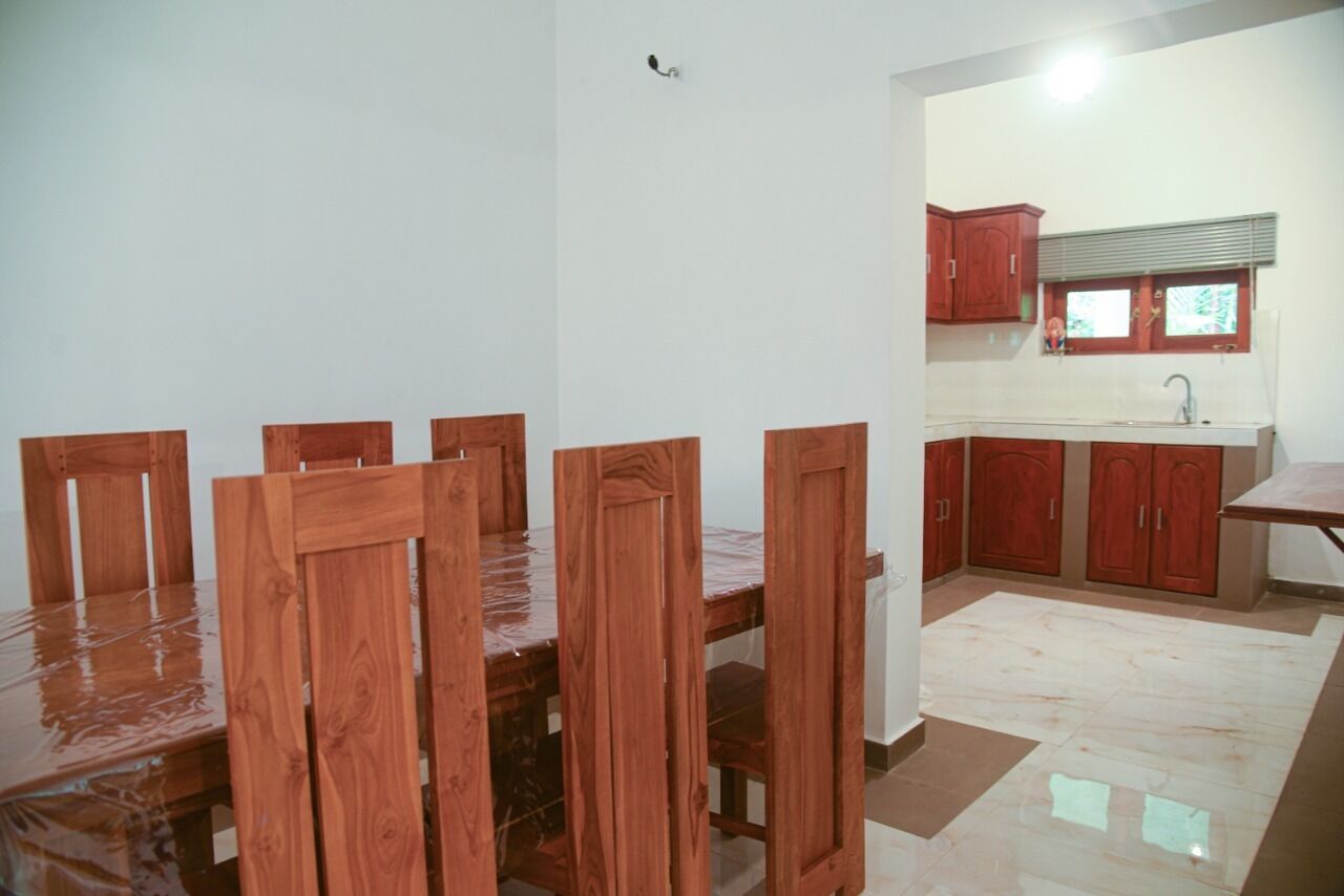 A dining area with a wooden table and chairs, a kitchen with red cabinets, and a tiled floor.