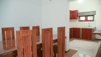 A dining area with a wooden table and chairs, a kitchen with red cabinets, and a tiled floor.