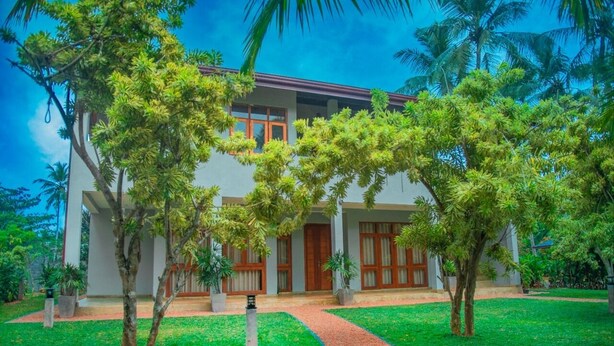 A two-story building with a covered patio and a curved pathway leading to the entrance. - Villa Mandari (Dharga Town)