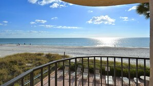 Blick auf einen Strand vom Balkon mit Geländer, bewölkter Himmel und dem Meer.