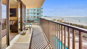 Ein Balkon mit Blick auf den Strand, ein Pool und ein Gebäude mit mehreren Balkonen.