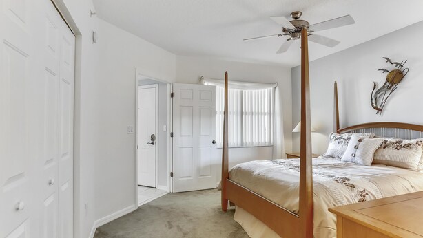 Une chambre à coucher avec un lit à baldaquin, un ventilateur de plafond et une porte donnant sur une autre pièce.