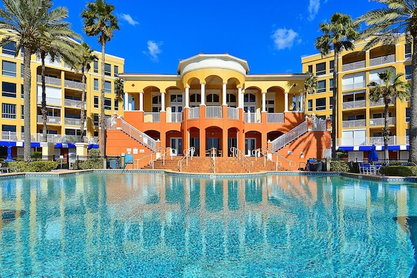Ett hotell med en stor pool, flera balkonger och palmer.