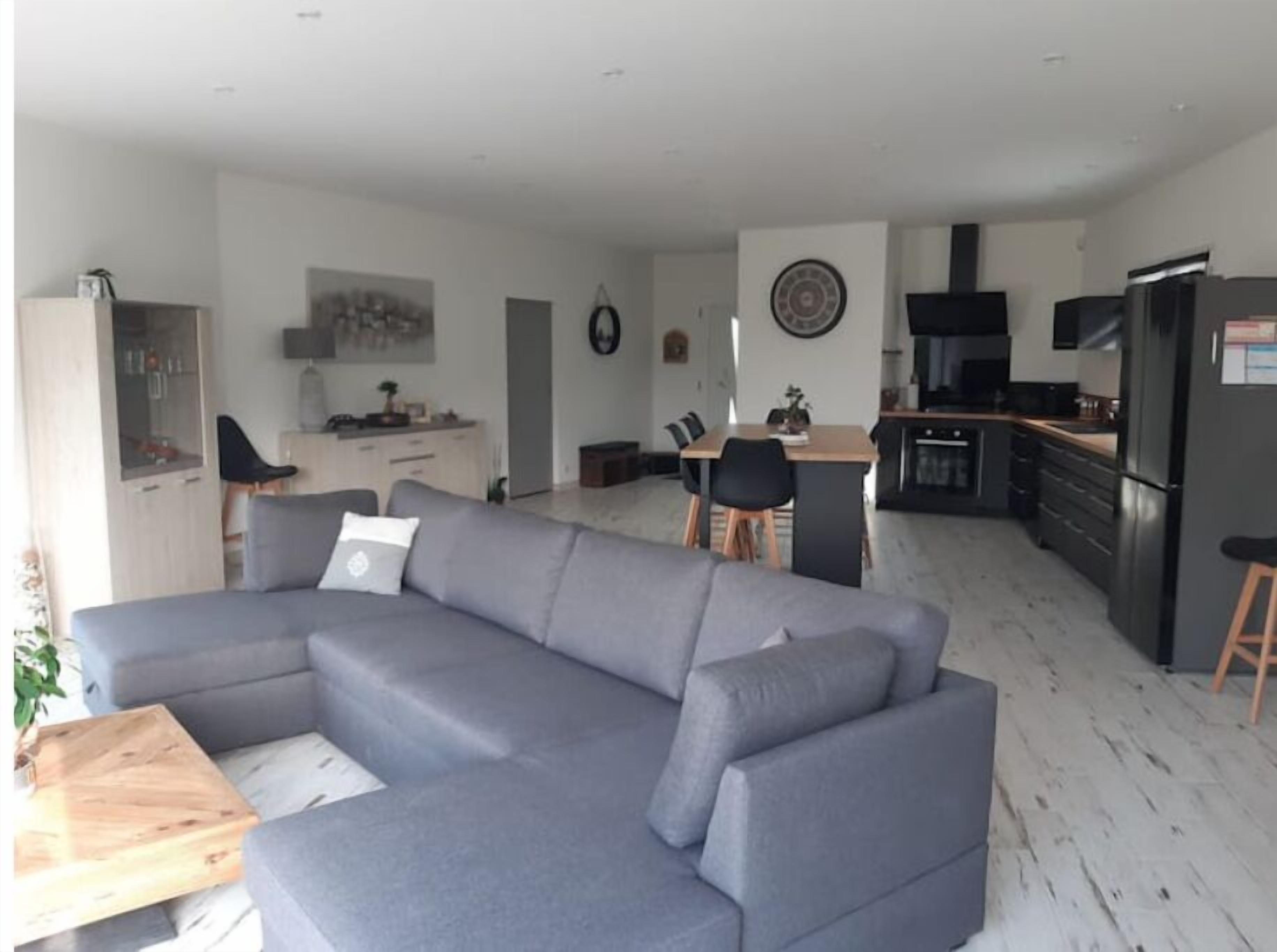 Un soggiorno moderno con un divano ad angolo grigio, un tavolino in legno e una zona pranzo con tavolo e sedie in legno.