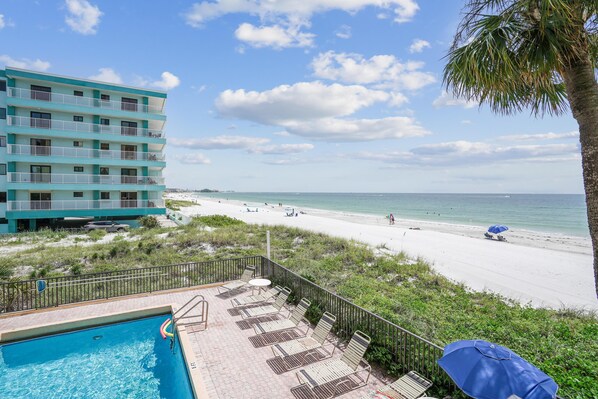 Relax by the pool surrounded by lounge chairs and a table, with the beach just steps away.