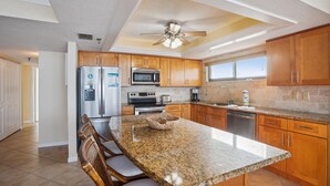 A modern kitchen with granite countertops, wooden cabinets, a built-in microwave, and a large island with seating. - Trillium 2A - Premier (Madeira Beach)