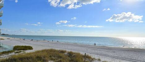 A beach view with a clear sky, sandy beach, and a building in the background.
