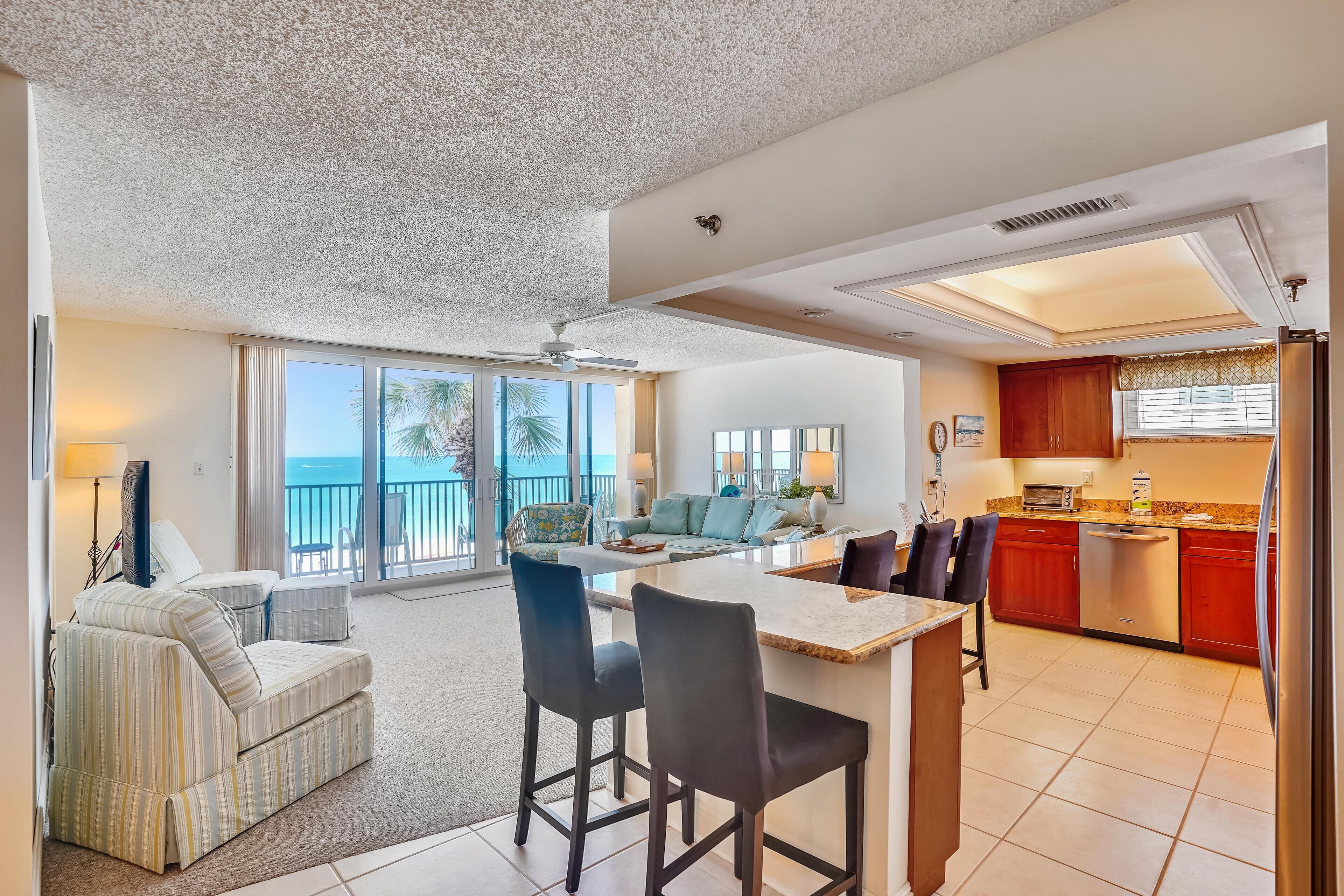 A spacious living area with a large window overlooking the ocean, a kitchen with red cabinets, and a dining area with a bar.