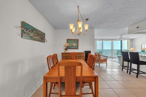A dining area with a wooden table, chairs, a chandelier, a painting, and a view of the outside. - Trillium 2C - Premier (Madeira Beach)
