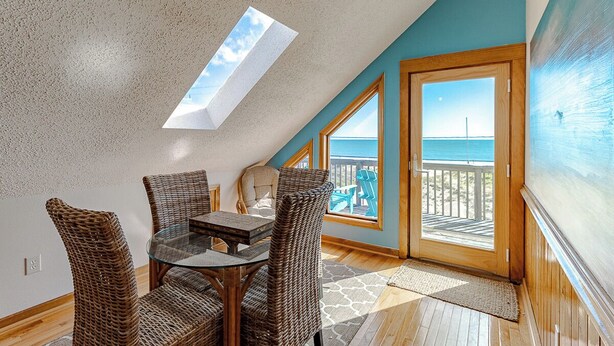 A room with a glass table, wicker chairs, a view of the ocean, and a skylight. - Sun Realty pet-friendly semi-oceanfront home with incredible views! (Kill Devil Hills)