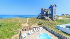 Une propriété située en bord de mer, comprenant une grande maison, une piscine et une terrasse avec des chaises longues.