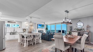 A spacious living area with a large TV, a dining table, and a view of the ocean.