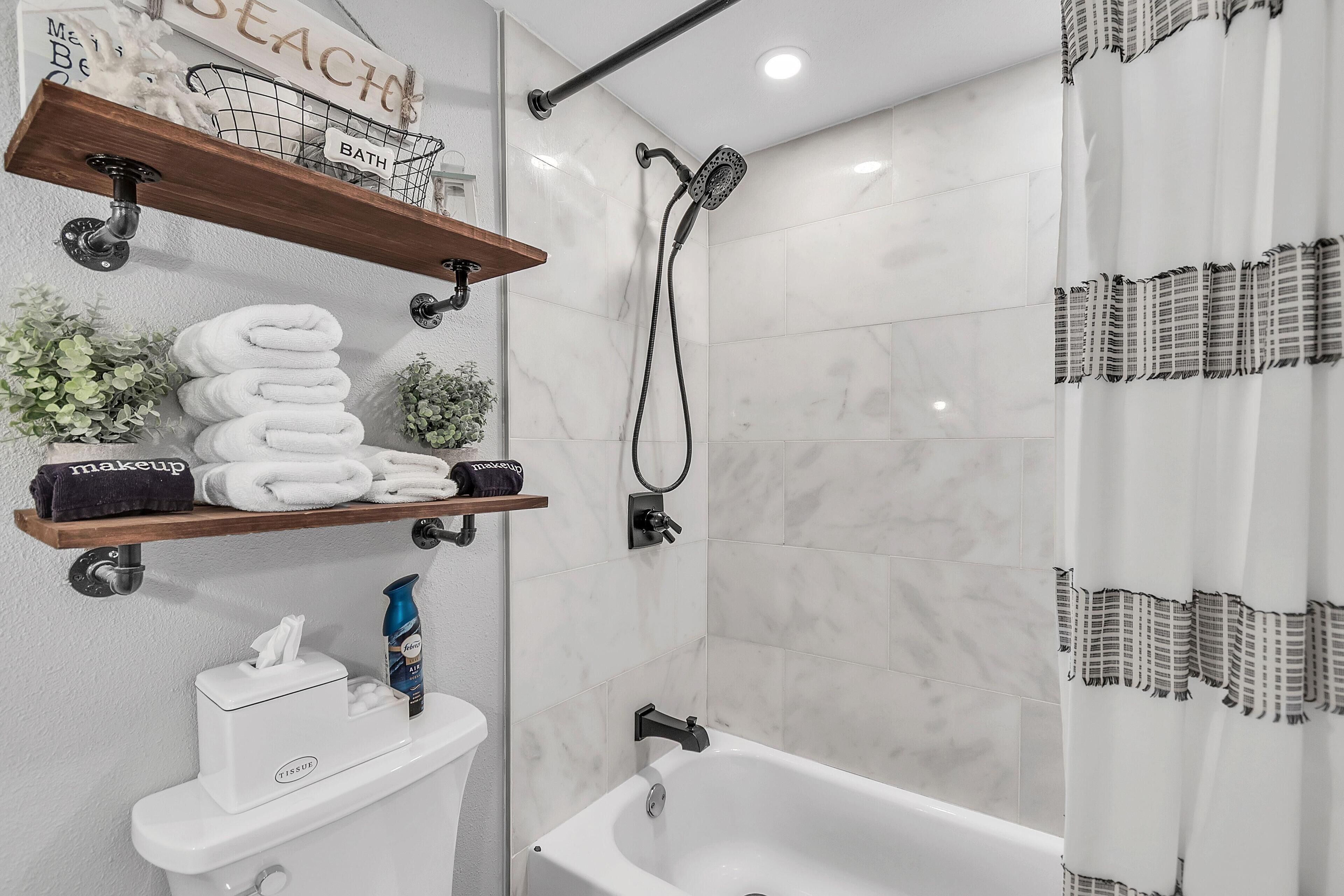 A bathroom with a bathtub, a shower, a towel rack with towels, a shelf with toiletries, and a toilet.