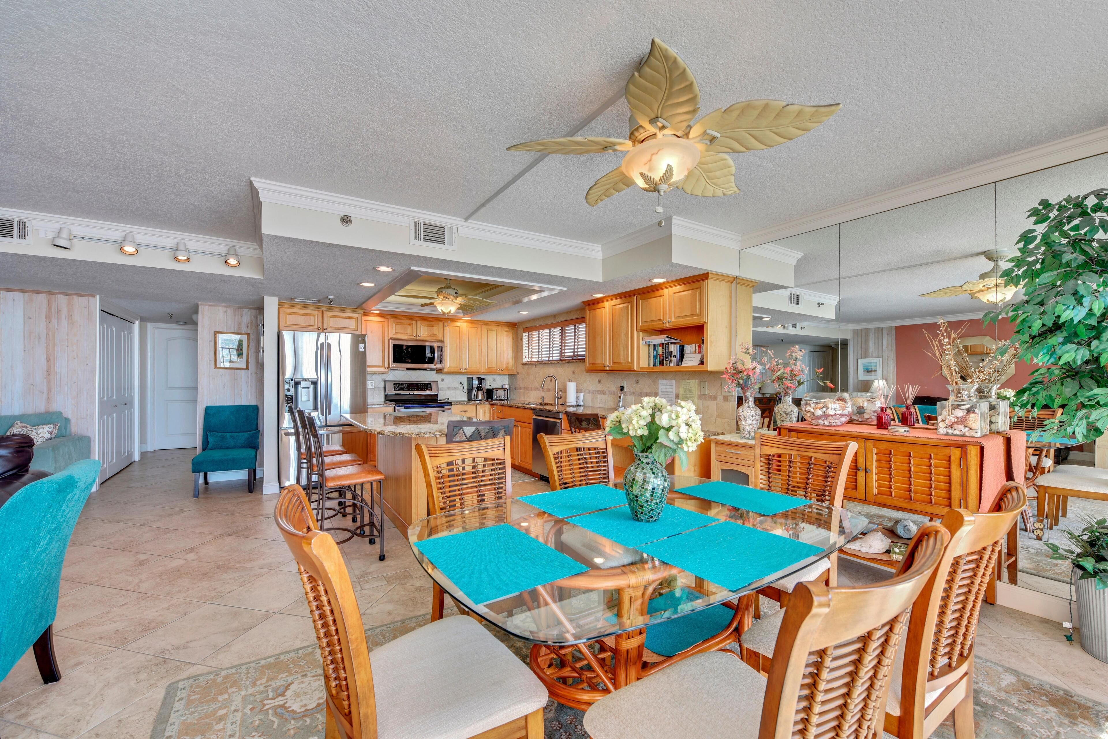 A spacious kitchen with wooden cabinets, a central island, and a dining area with a glass table and wicker chairs.