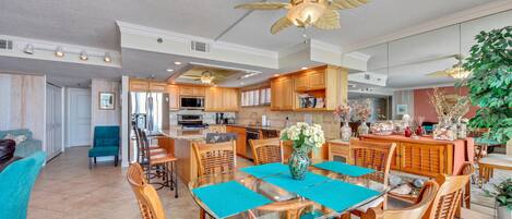 A spacious kitchen with wooden cabinets, a central island, and a dining area with a glass table and wicker chairs.