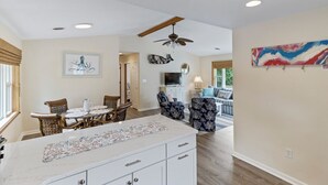 A spacious living area with a dining table, chairs, a sofa, and a ceiling fan. - Sun Realty pet-friendly soundside home with private pool! (Kill Devil Hills)