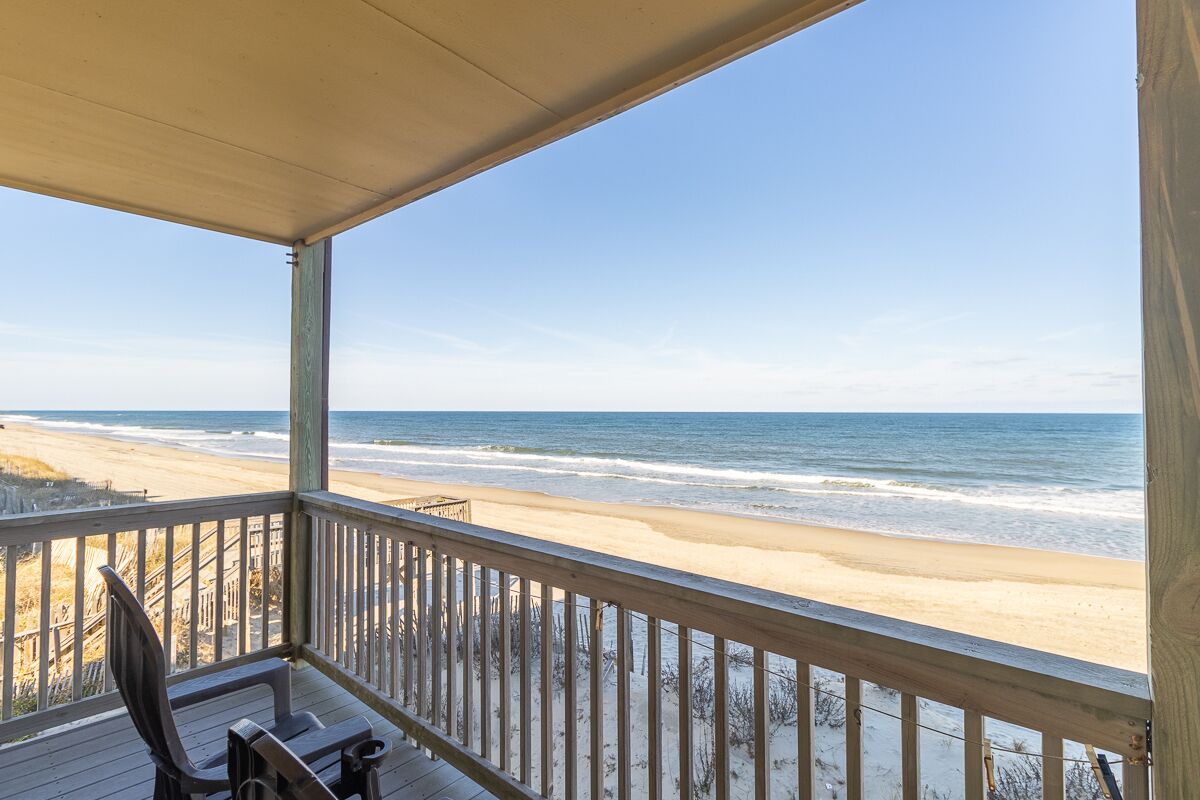 Una terraza de madera con vista a la playa y el océano.