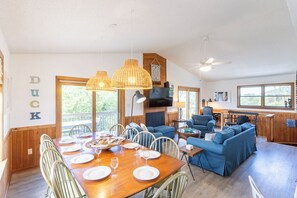 Un vaste espace de vie comprenant une table à manger en bois, mise pour le repas, un canapé bleu et un téléviseur.