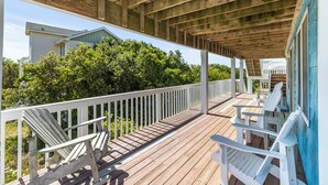 Une terrasse en bois, agrémentée de rampes blanches et de fauteuils Adirondack, qui offre une vue imprenable sur un paysage verdoyant.