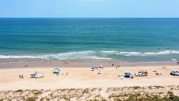 Une plage avec un ciel dégagé, une mer calme et des gens qui profitent de l’eau.