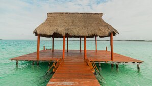 A wooden pier leading to a thatched-roof structure over calm turquoise waters.