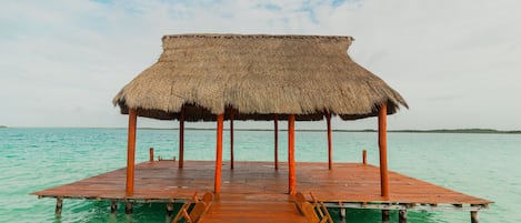 A wooden pier leading to a thatched-roof structure over calm turquoise waters.