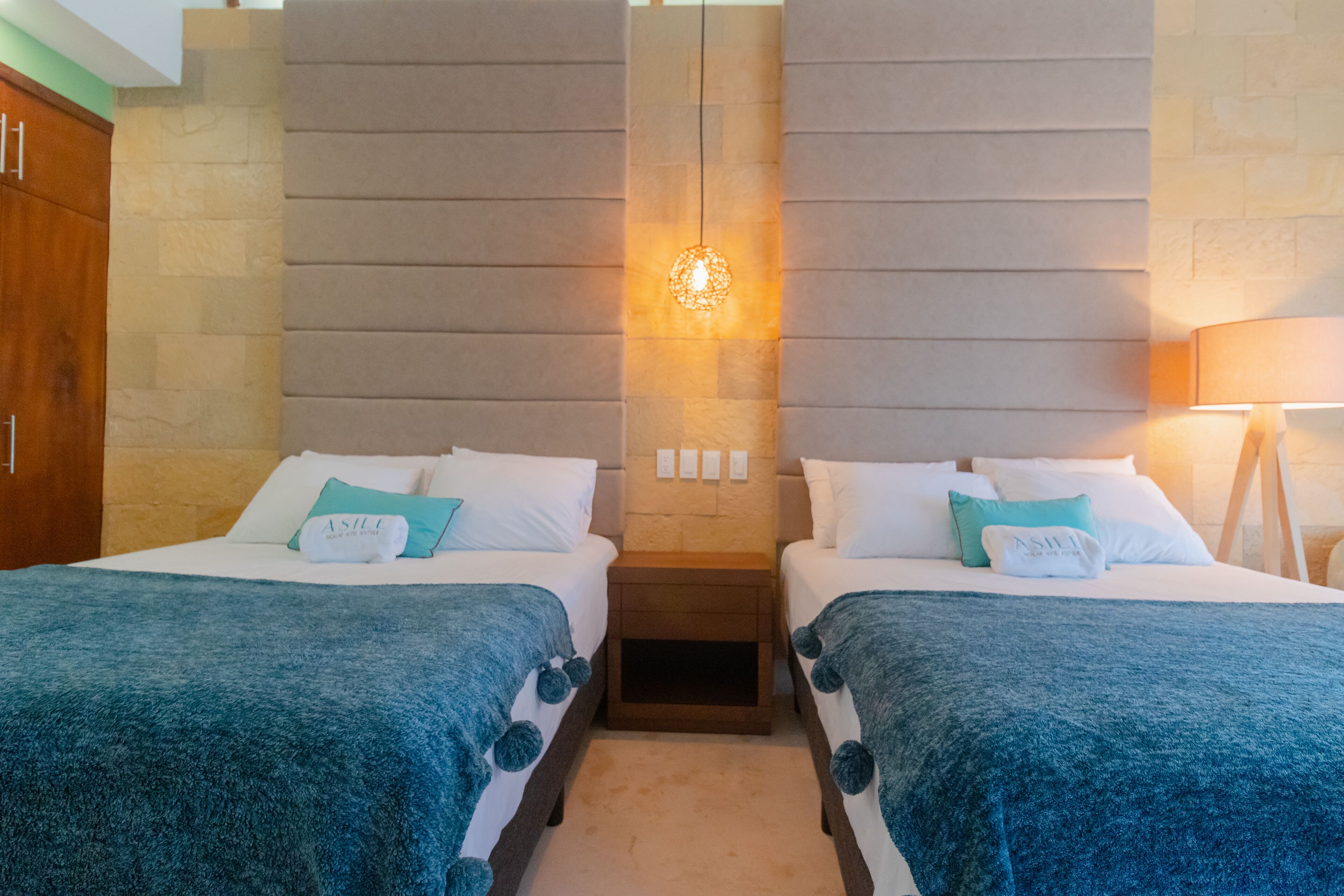 Une chambre d’hôtel avec deux lits, un mur décoratif en pierre et un luminaire suspendu.