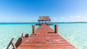 A wooden pier leading to a thatched-roof structure over turquoise waters.