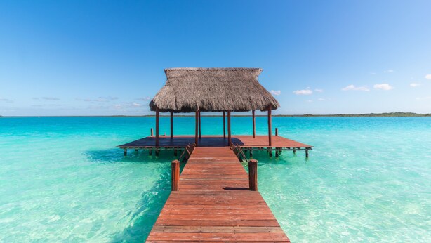 A wooden pier leading to a thatched-roof structure over clear turquoise water.