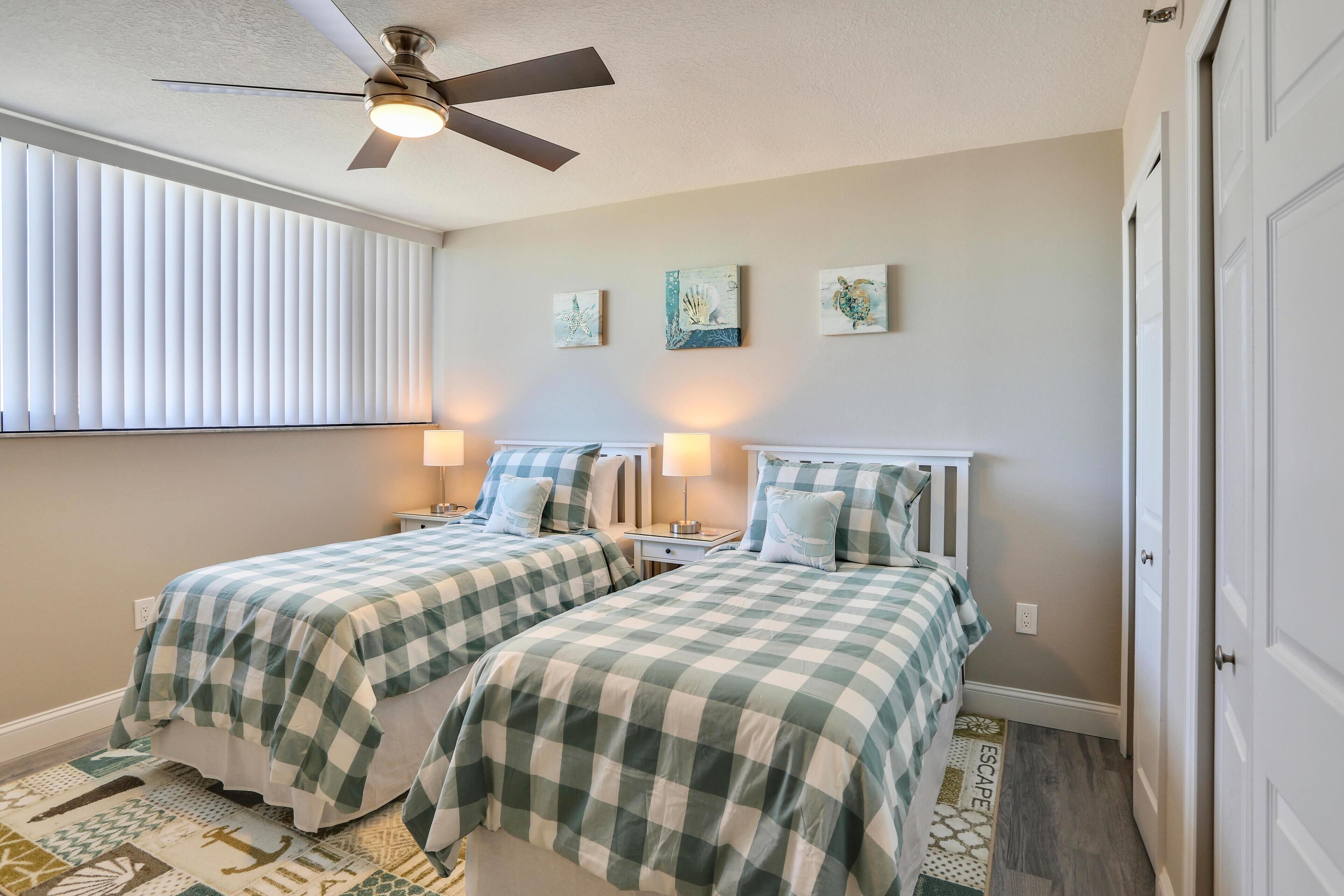 A bedroom with two beds, a ceiling fan, and artwork on the wall.