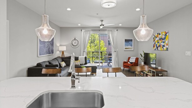A modern kitchen with a large island, a dining area with a table and chairs, and a living room with a sofa and a TV. - Chic 2BR Apt, Steps from N Main St, Balcony View
 (Greenville)