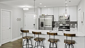 A modern kitchen with white cabinetry, stainless steel appliances, and bar stools. - Chic 2BR Apt, Steps from N Main St, Balcony View
 (Greenville)