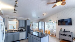 Een moderne keuken met grijze kastjes, een centraal eiland en een eethoek met houten stoelen.