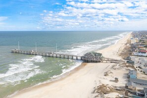 A coastal area with a pier extending into the sea, a beach, and adjacent buildings.