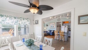 Een eethoek met een witte tafel voor zes personen, een plafondventilator en uitzicht op de keuken.