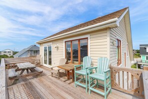 A wooden deck with a table and chairs, a covered patio area, and a house with large windows and a door. - Oceanside home in South Nags Head just 250 ft to the beach!! (South Nags Head)