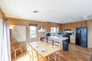 Une cuisine avec des meubles de rangement en bois, une table à manger avec des chaises, un réfrigérateur noir et un ventilateur de plafond.