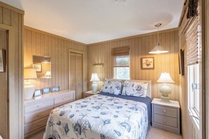 Ein Schlafzimmer mit einem Bett, Nachttischen, einer Kommode und einem Fenster mit Jalousien.