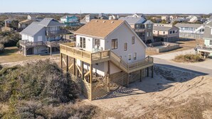 A beachfront house with a wooden deck and a second-story balcony, surrounded by other similar houses.