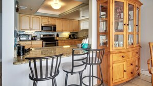 Una cocina con encimeras de granito, gabinetes de madera, microondas integrado y un mueble de madera con puertas de vidrio.